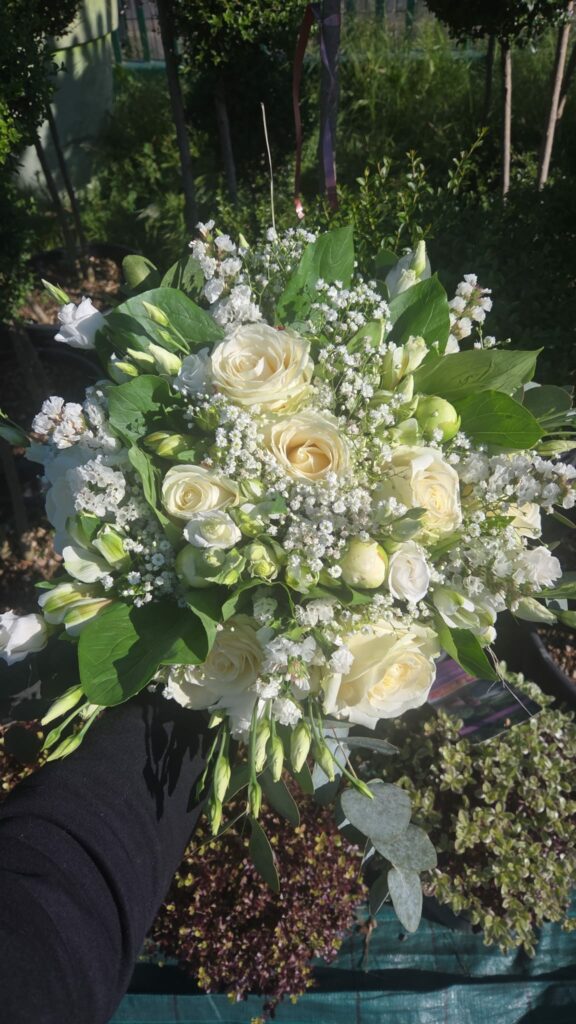 Bouquet de mariée ivoire tenu à la main : roses crème, lisianthus blancs, alstroemerias, statice et gypsophile sur un feuillage vert franc