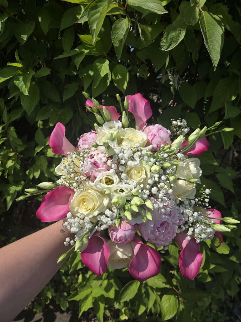 Bouquet de mariée rose et blanc tenu à la main : arums fuchsia, pivoines roses, roses ivoire, lisianthus et gypsophile