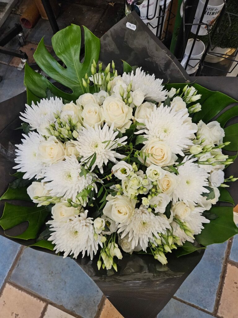 Bouquet rond entièrement blanc : chrysanthèmes, roses et lisianthus blancs sur un feuillage de monstera, emballage noir