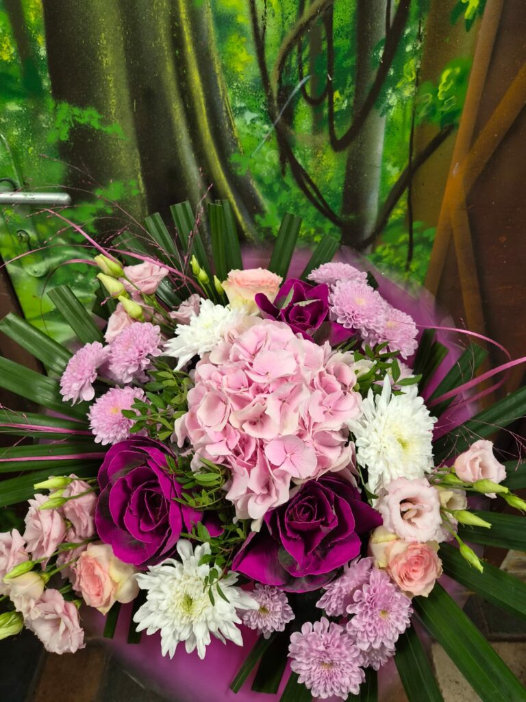 Bouquet rond rose et fuchsia : hortensia rose pâle, roses pourpres, chrysanthèmes mauves et blancs, lisianthus rose poudré, dans un papier rose