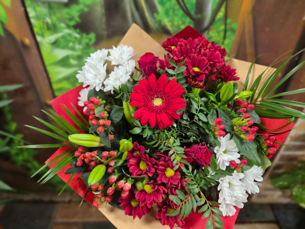 Bouquet rouge et blanc : gerbera rouge, chrysanthèmes bordeaux et blancs, roses rouges et baies d'hypericum, dans un papier rouge et kraft