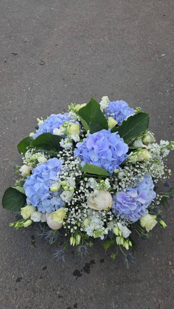 Composition florale ronde bleue et blanche : hortensias bleus, pivoines crème, roses blanches, lisianthus, giroflées, gypsophile et chardons bleus