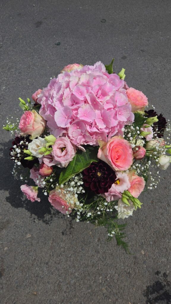 Composition florale ronde aux tons roses : hortensia rose, roses pâles, lisianthus, dahlias pourpre foncé et gypsophile