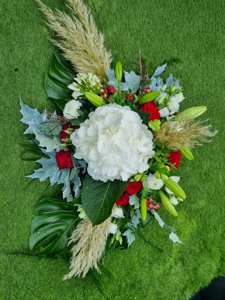 Gerbe florale blanche et rouge : hortensia blanc au centre, roses rouges, lis, baies d'hypericum, plumes de pampa et feuilles de monstera