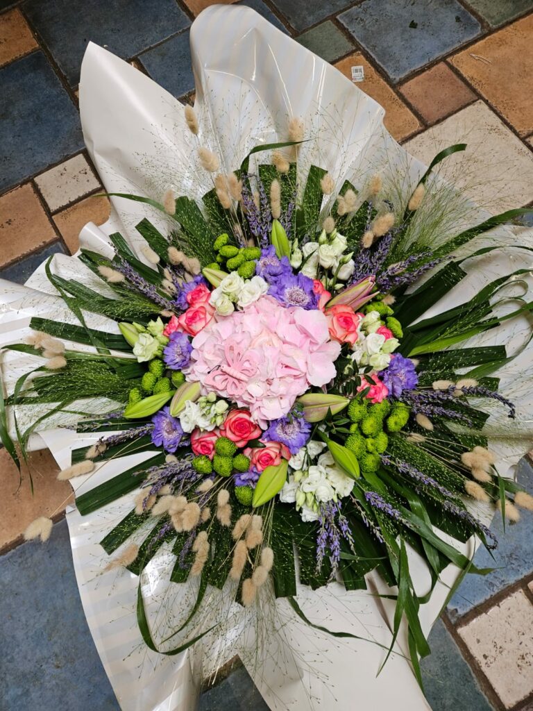 Grande composition ronde rose et mauve : hortensia rose au centre, roses fuchsia, scabieuses violettes, lisianthus blancs, lavande séchée et lagurus, sur un éventail de feuillage vert
