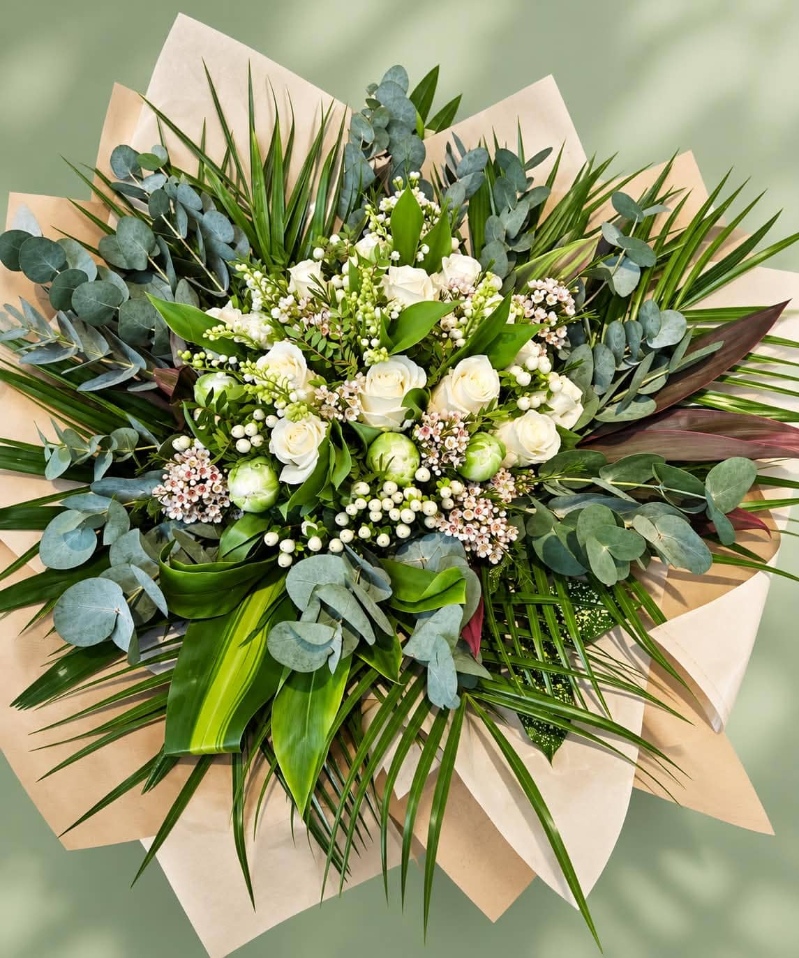 Bouquet rond de roses blanches, symphorine, eucalyptus et palmes, emballé dans un papier kraft